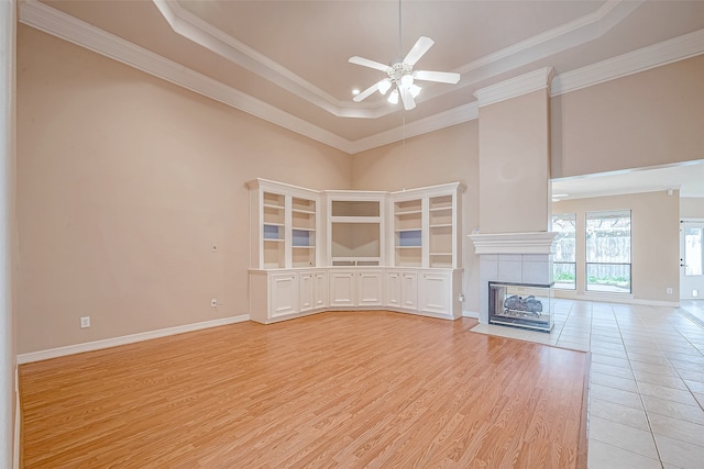 unfurnished living room with crown molding, ceiling fan, light wood-type flooring, a fireplace, and a tray ceiling