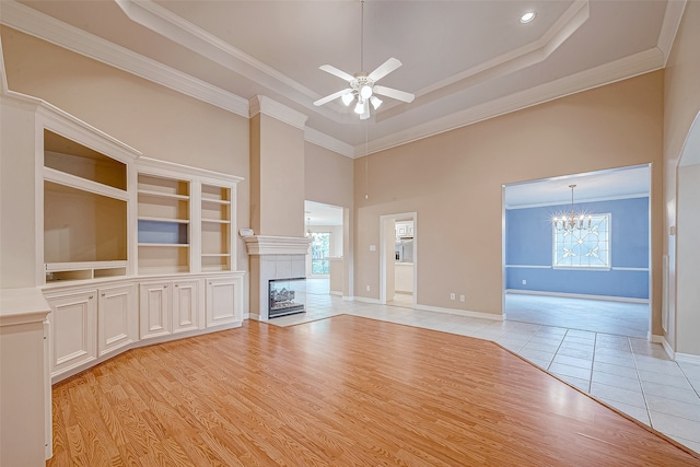 unfurnished living room with a tile fireplace, a towering ceiling, light hardwood / wood-style floors, ceiling fan with notable chandelier, and ornamental molding