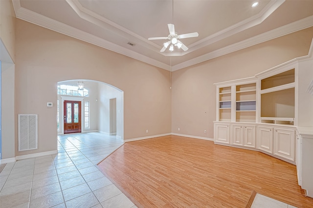 empty room with a raised ceiling, light hardwood / wood-style flooring, ceiling fan, and crown molding