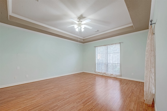 empty room with a raised ceiling, ceiling fan, light hardwood / wood-style flooring, and ornamental molding