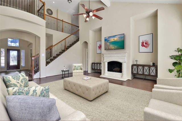 living area with arched walkways, a fireplace with raised hearth, wood finished floors, a towering ceiling, and stairs