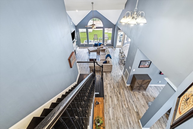 staircase with high vaulted ceiling, wood-type flooring, and ceiling fan with notable chandelier