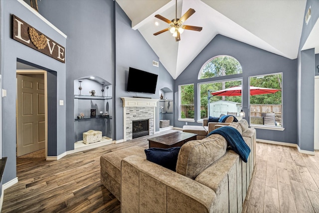 living room featuring ceiling fan, hardwood / wood-style flooring, a stone fireplace, and high vaulted ceiling