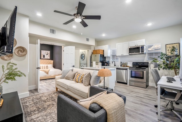 living area with light wood-style floors, visible vents, stacked washer and dryer, and recessed lighting