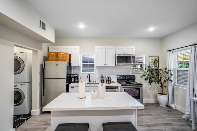 kitchen featuring light stone countertops, stainless steel appliances, stacked washer and clothes dryer, light hardwood / wood-style floors, and white cabinetry