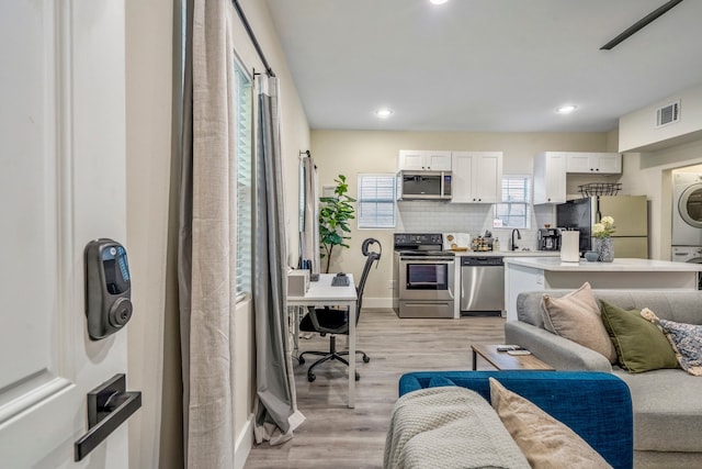 living room with stacked washer / dryer, sink, and light hardwood / wood-style floors