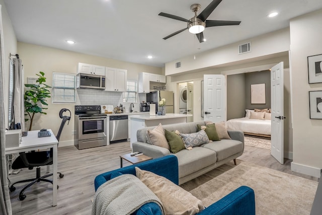 living room with sink, light wood-type flooring, stacked washer / dryer, and ceiling fan