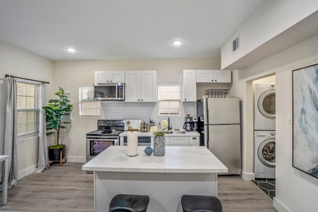 kitchen with white cabinets, stacked washing maching and dryer, light wood-type flooring, and stainless steel appliances