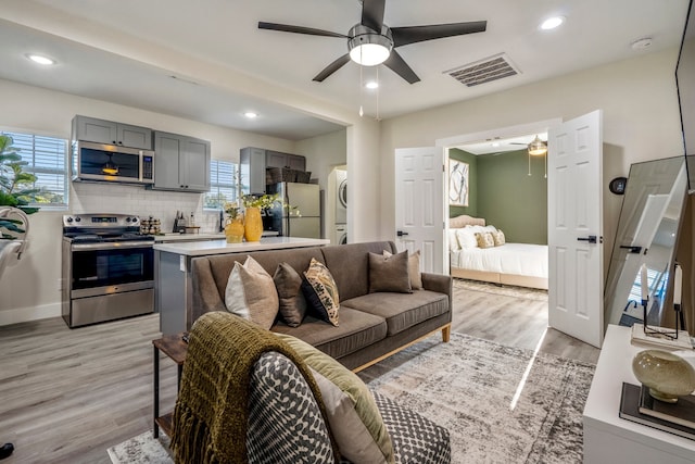 living room with ceiling fan, light hardwood / wood-style flooring, and stacked washer and clothes dryer