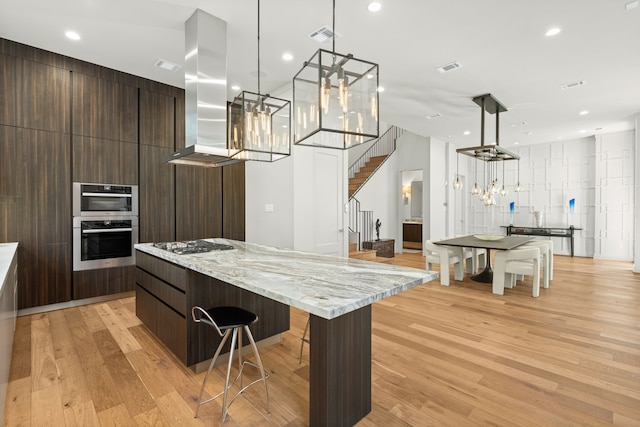 kitchen with pendant lighting, light wood-type flooring, island range hood, and a spacious island