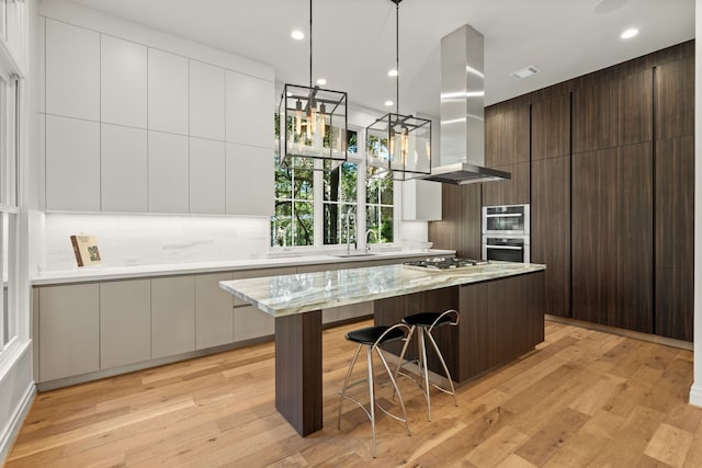 kitchen featuring island range hood, dark brown cabinets, a spacious island, and light wood-type flooring