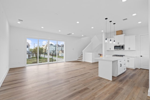 kitchen featuring appliances with stainless steel finishes, pendant lighting, light hardwood / wood-style flooring, white cabinets, and a kitchen island