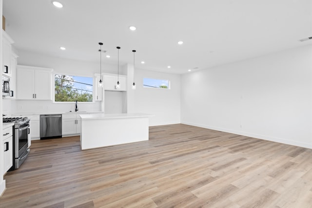 kitchen featuring white cabinetry, a kitchen island, appliances with stainless steel finishes, light hardwood / wood-style floors, and decorative light fixtures