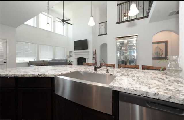 kitchen featuring light stone countertops, a towering ceiling, stainless steel dishwasher, ceiling fan, and pendant lighting