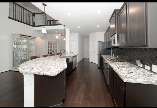 kitchen with dark wood-type flooring, a center island with sink, appliances with stainless steel finishes, decorative light fixtures, and dark brown cabinets