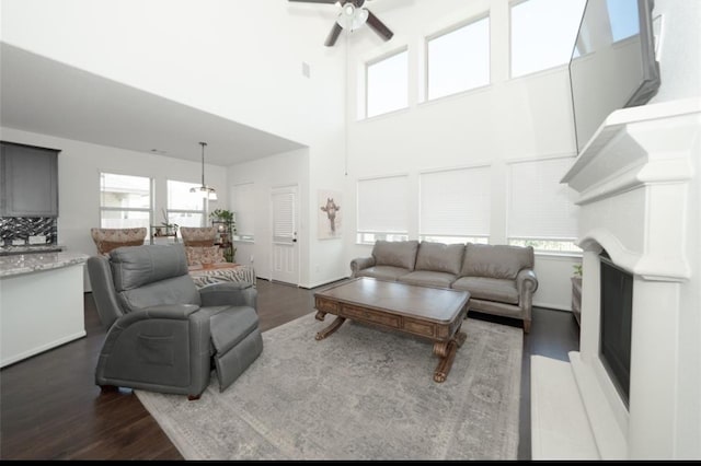 living room with ceiling fan, dark wood-type flooring, a towering ceiling, and a healthy amount of sunlight