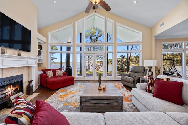 living room featuring high vaulted ceiling, ceiling fan, wood-type flooring, and a tile fireplace