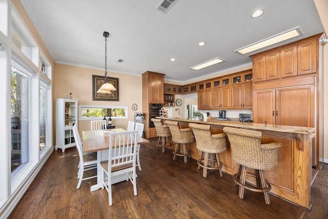 kitchen featuring decorative light fixtures, ornamental molding, dark wood-type flooring, and a kitchen breakfast bar