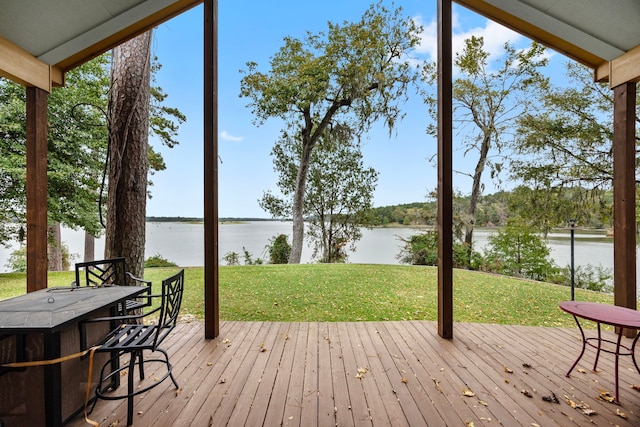 wooden terrace featuring a bar, a water view, and a lawn