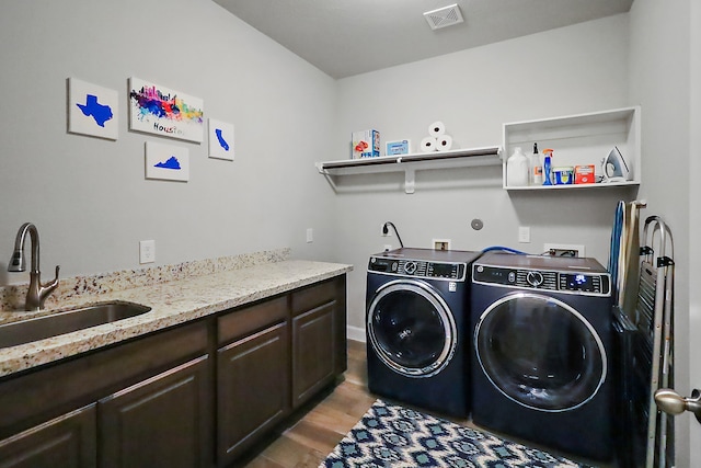 clothes washing area with washer and dryer, cabinets, light wood-type flooring, and sink