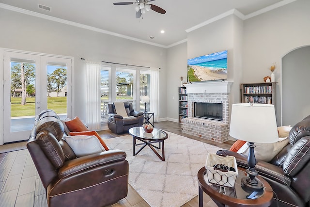 living room featuring ceiling fan, french doors, a brick fireplace, light hardwood / wood-style floors, and ornamental molding