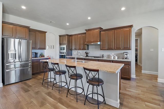 kitchen featuring hardwood / wood-style floors, a breakfast bar, a kitchen island with sink, sink, and appliances with stainless steel finishes