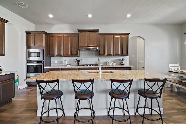 kitchen featuring sink, stainless steel appliances, dark hardwood / wood-style flooring, an island with sink, and decorative backsplash