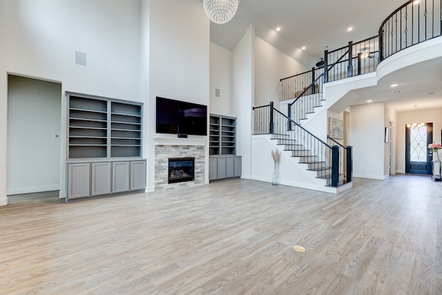 unfurnished living room featuring a stone fireplace, light wood-type flooring, a towering ceiling, and an inviting chandelier