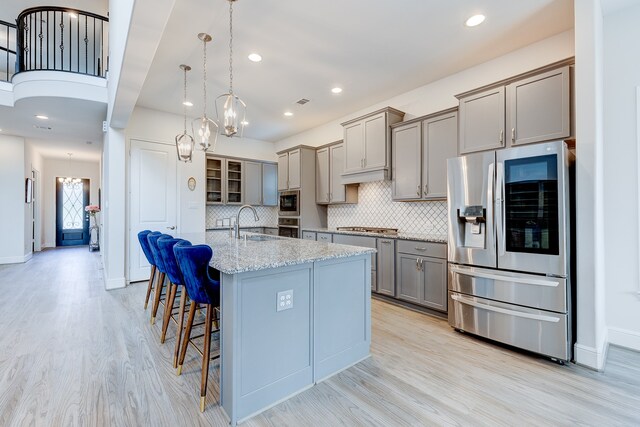 kitchen featuring a kitchen breakfast bar, sink, hanging light fixtures, appliances with stainless steel finishes, and light hardwood / wood-style floors