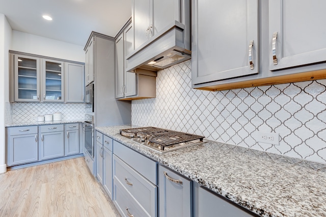 kitchen with light stone countertops, appliances with stainless steel finishes, tasteful backsplash, light hardwood / wood-style floors, and custom range hood