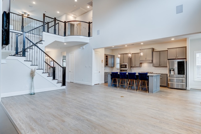 kitchen featuring a center island, a towering ceiling, appliances with stainless steel finishes, light hardwood / wood-style floors, and a kitchen bar