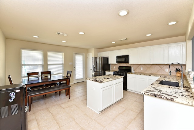 kitchen with light stone countertops, white cabinetry, sink, a kitchen island, and black appliances