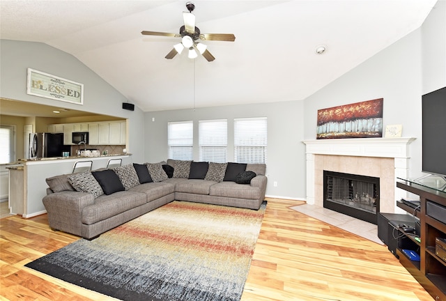 living room featuring light wood-type flooring, high vaulted ceiling, ceiling fan, and a tiled fireplace