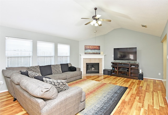 living room with hardwood / wood-style floors, ceiling fan, lofted ceiling, and a tiled fireplace