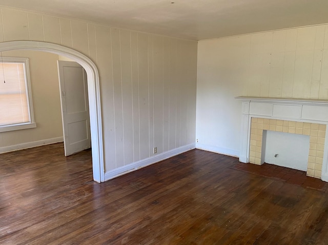 unfurnished living room featuring wood walls, dark wood-type flooring, and a tiled fireplace