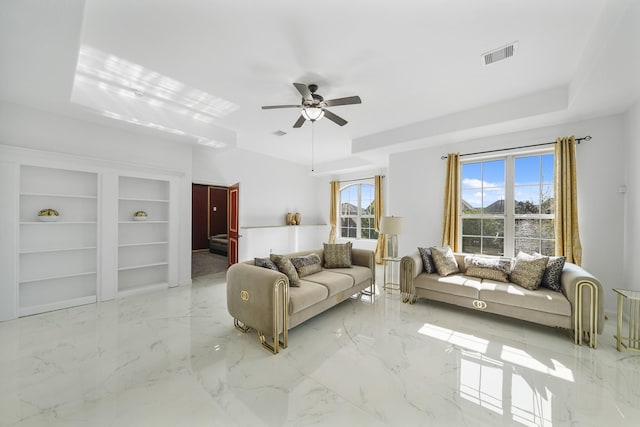 living room with ceiling fan, a raised ceiling, and built in features