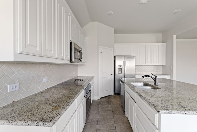 kitchen with light stone counters, stainless steel appliances, sink, white cabinetry, and an island with sink