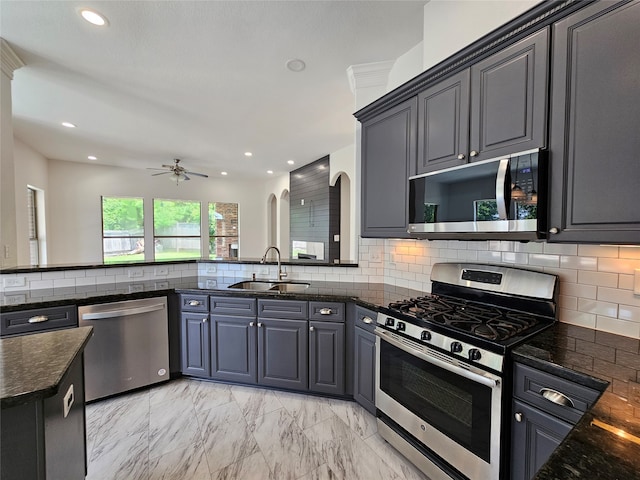 kitchen with tasteful backsplash, stainless steel appliances, ceiling fan, sink, and dark stone countertops