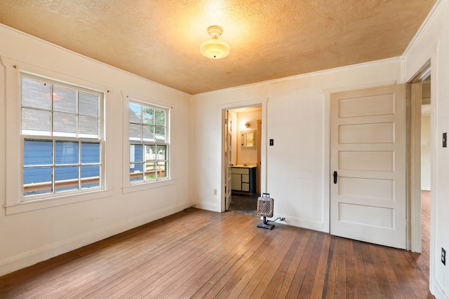 unfurnished bedroom featuring crown molding, ensuite bathroom, wood-type flooring, and a textured ceiling