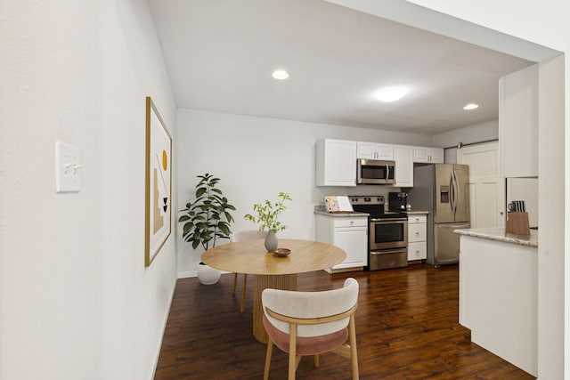 kitchen featuring light stone countertops, white cabinetry, dark wood-type flooring, a barn door, and appliances with stainless steel finishes