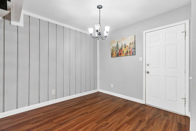 unfurnished room with wood walls, dark wood-type flooring, and a notable chandelier