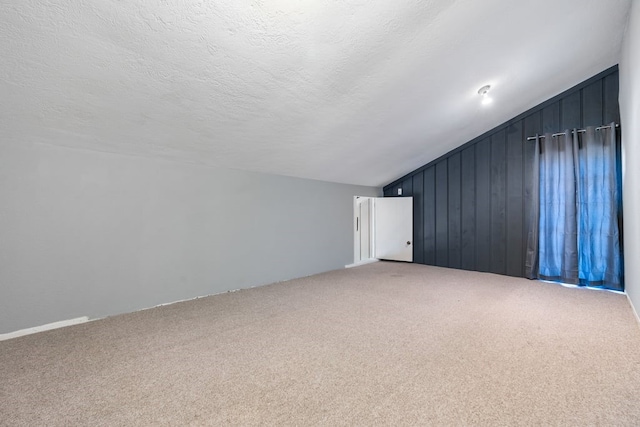 bonus room with carpet flooring, a textured ceiling, wooden walls, and vaulted ceiling