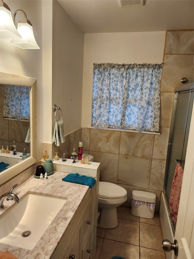 full bathroom featuring tile patterned flooring, combined bath / shower with glass door, toilet, vanity, and tile walls