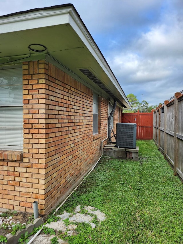 view of side of property featuring central air condition unit, fence, a lawn, and brick siding