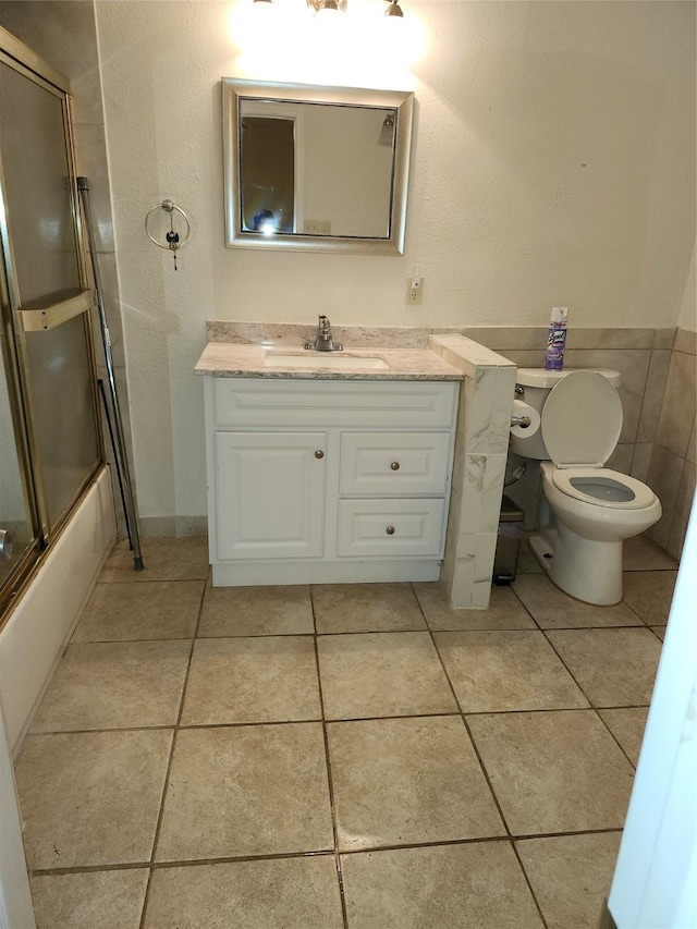 bathroom featuring vanity, combined bath / shower with glass door, tile patterned flooring, and toilet