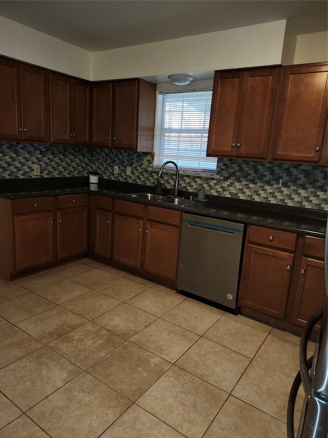 kitchen with light tile patterned floors, a sink, dishwasher, tasteful backsplash, and dark countertops