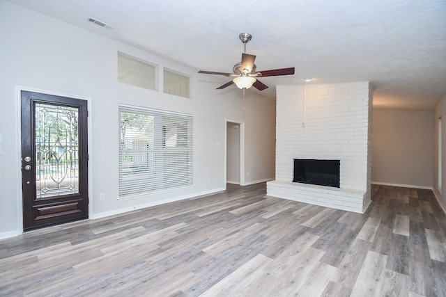 unfurnished living room featuring vaulted ceiling, ceiling fan, a brick fireplace, and light hardwood / wood-style floors