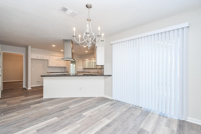 kitchen featuring kitchen peninsula, pendant lighting, island exhaust hood, light hardwood / wood-style floors, and white cabinets