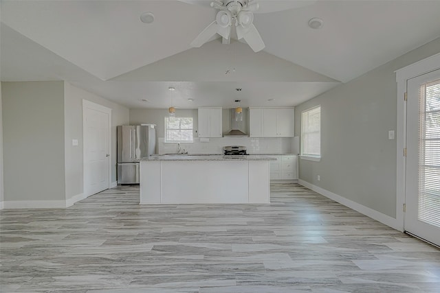 kitchen featuring lofted ceiling, white cabinets, wall chimney range hood, appliances with stainless steel finishes, and a kitchen island