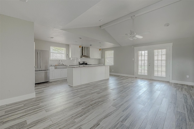 kitchen with appliances with stainless steel finishes, wall chimney exhaust hood, white cabinetry, vaulted ceiling with beams, and a kitchen island